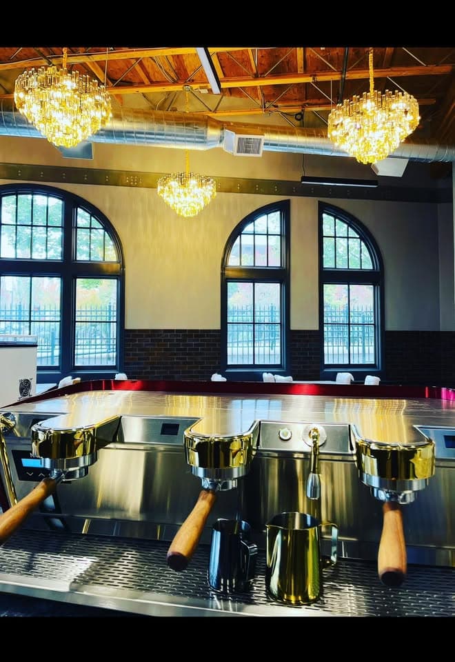 The gold espresso machine beneath chandeliers and arched windows at Legacy Coffee